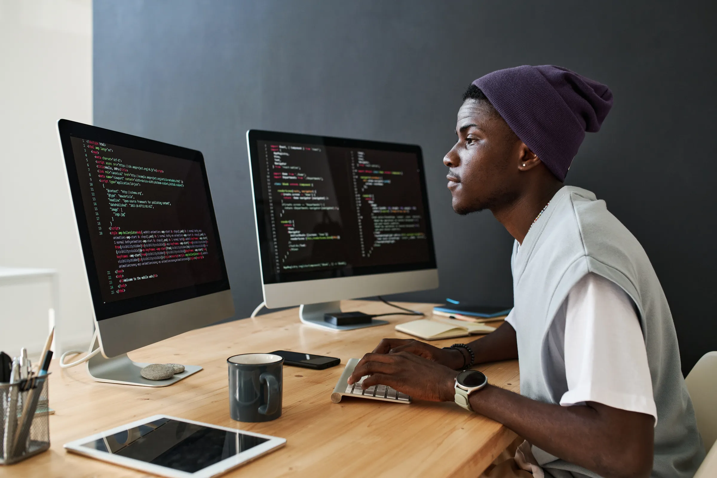 Jeune développeur en bonnet, futur ingénieur en informatique, codant sur deux écrans dans un espace de travail lumineux
